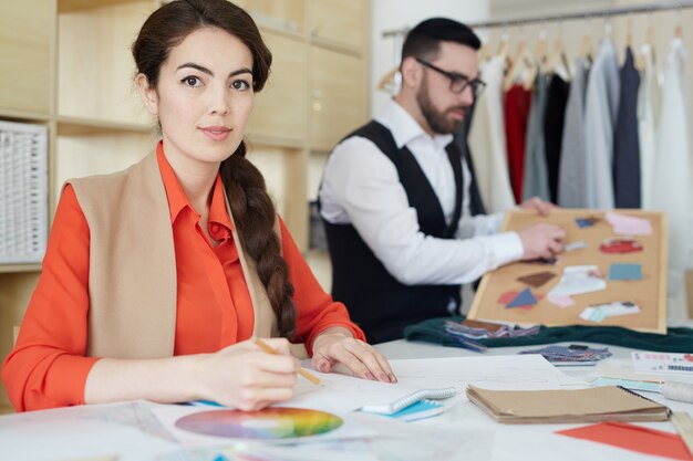 Creative designer planning clothing concepts with a color palette and sketches in a modern fashion workspace.