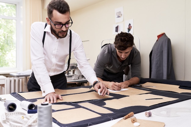 Fashion designers working together on fabric patterns at a studio table with sewing tools and garment samples.