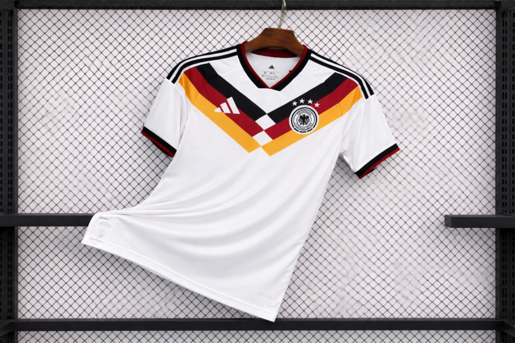 An Adidas Germany soccer shirt is displayed on a wooden hanger with the national crest and colorful diagonal design.