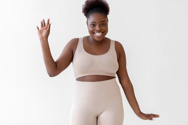 Smiling woman in beige body shaper posing confidently against white background.