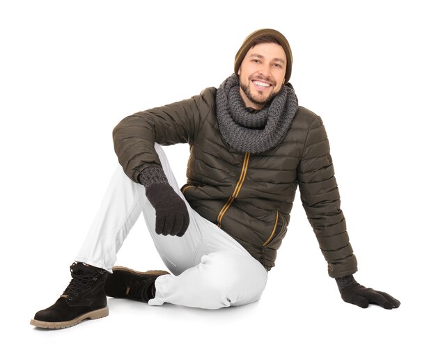 Man sitting on floor in winter outfit, wearing olive jacket, scarf, gloves, white pants and boots, smiling at the camera.