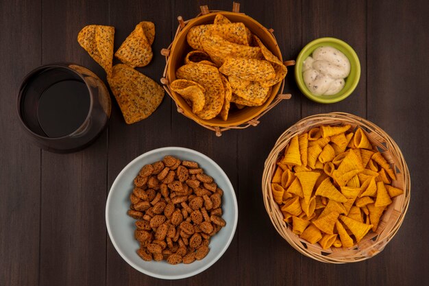 Top view of spicy chips, corn snacks, rusks and cola arranged on a wooden table.