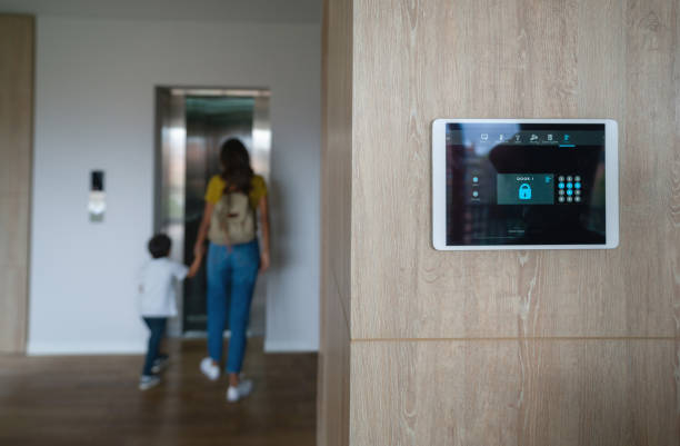 A digital security system is displayed on the wall while a parent and child head to the elevator in a residential space.