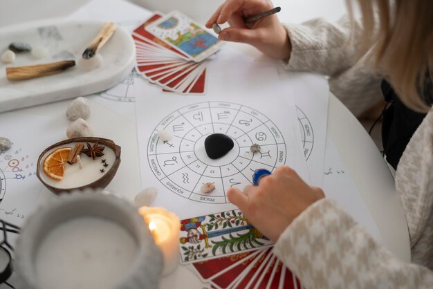 Person using tarot cards and a zodiac chart with candles and crystals on a table.