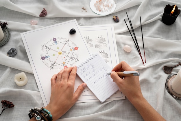 Hands writing notes beside a numerology chart with candles, crystals, and incense.